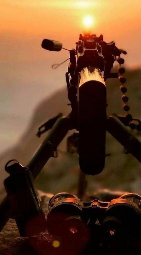 An assault rifle pointed toward the camera with a sunset in the background.