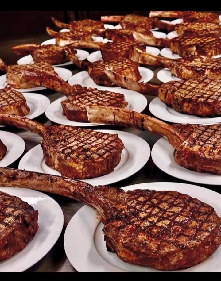 Many grilled Tomahawk steaks on white plates.