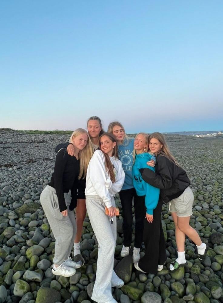 Six young women posing together on a rocky beach under a clear sky.
