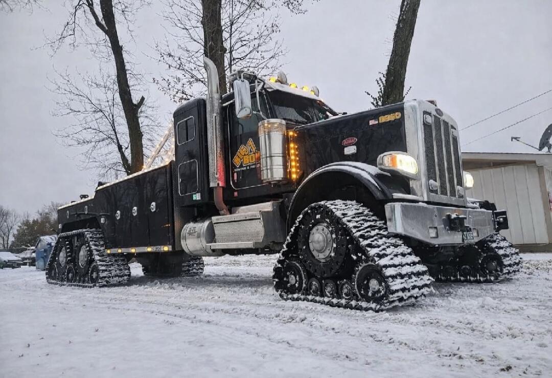 A large black heavy-duty truck with caterpillar tracks parked in snow.