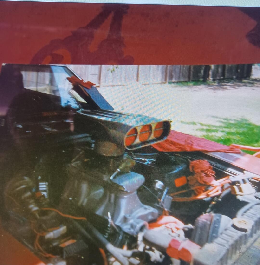 A car with an exposed engine bay featuring a large triple-helmet blower/supercharger protruding through the hood.