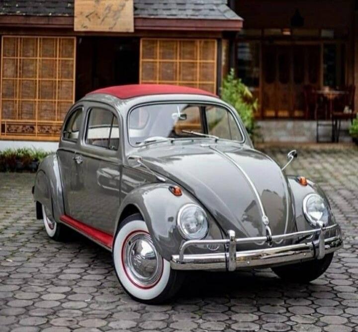 A classic Volkswagen Beetle with a red roof and red trim on the side, parked on a cobblestone driveway in front of a building with traditional Japanese architecture.