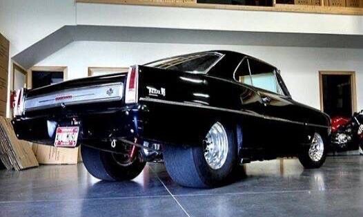 Black classic car in a garage, rear view with wide tires.