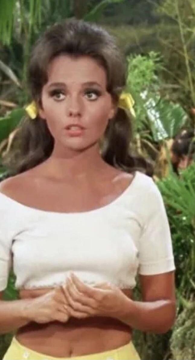 A woman wearing a white cropped top in a tropical outdoor setting.