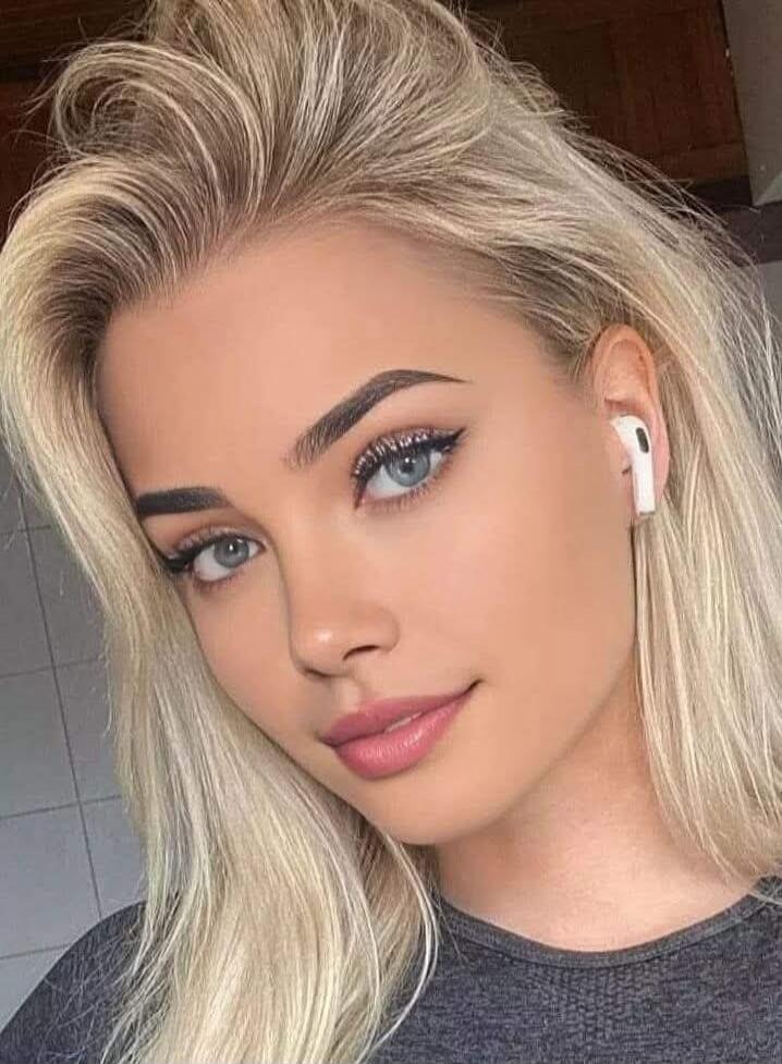 Portrait of a young woman with blonde hair and blue eyes, wearing white AirPods.