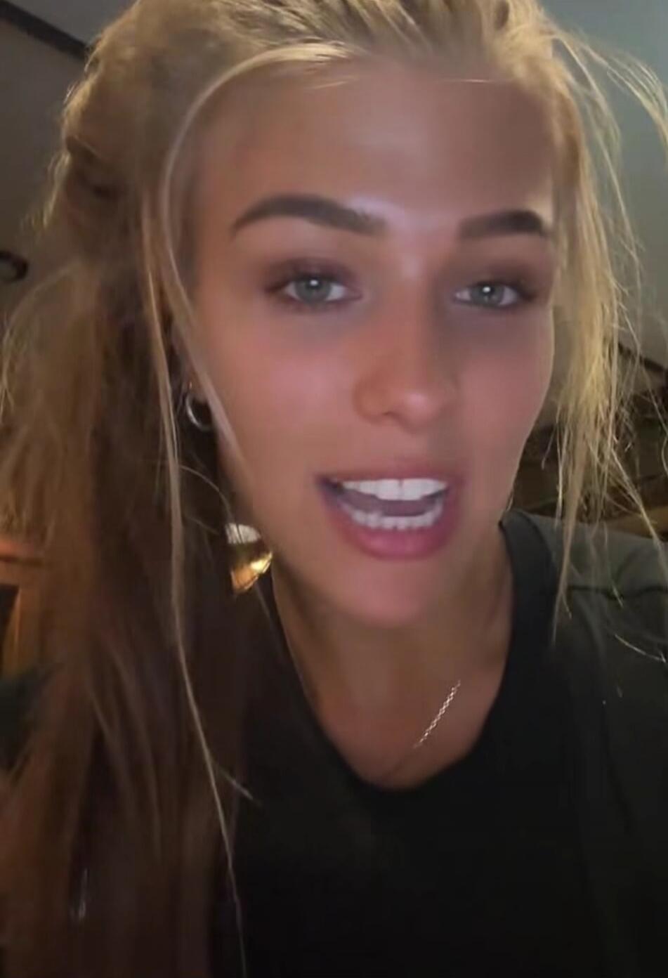 A young woman with blonde hair and light eyes is speaking directly to the camera.