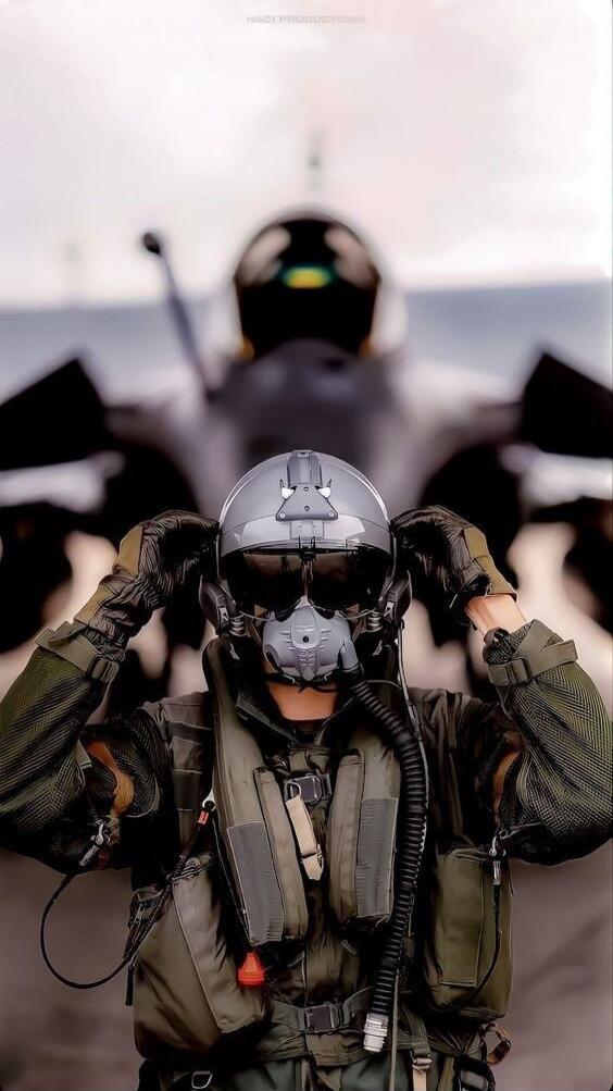 A fighter pilot in full gear puts on a helmet in front of a fighter jet.