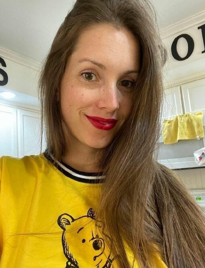 Woman with long brown hair wearing a yellow Winnie the Pooh shirt, smiling in a kitchen.