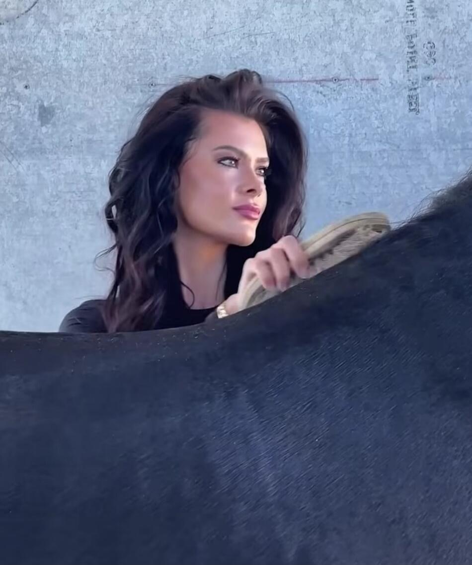A woman is brushing a dark animal, possibly a horse. Faint text 'MORE TOTAL' is visible in the background.