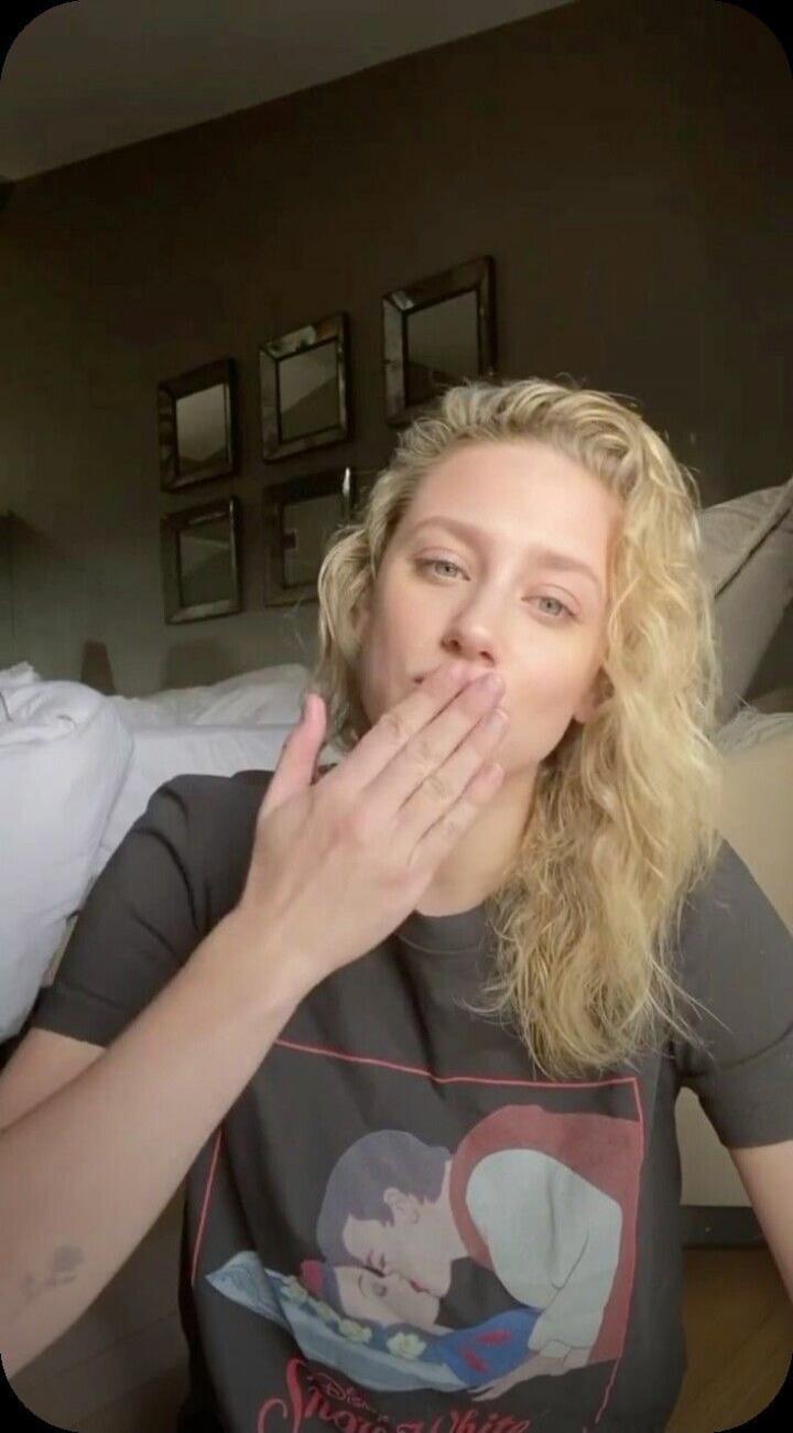A blonde woman blows a kiss to the camera. She is wearing a dark t-shirt with a Snow White print, depicting Prince Charming kissing Snow White.
