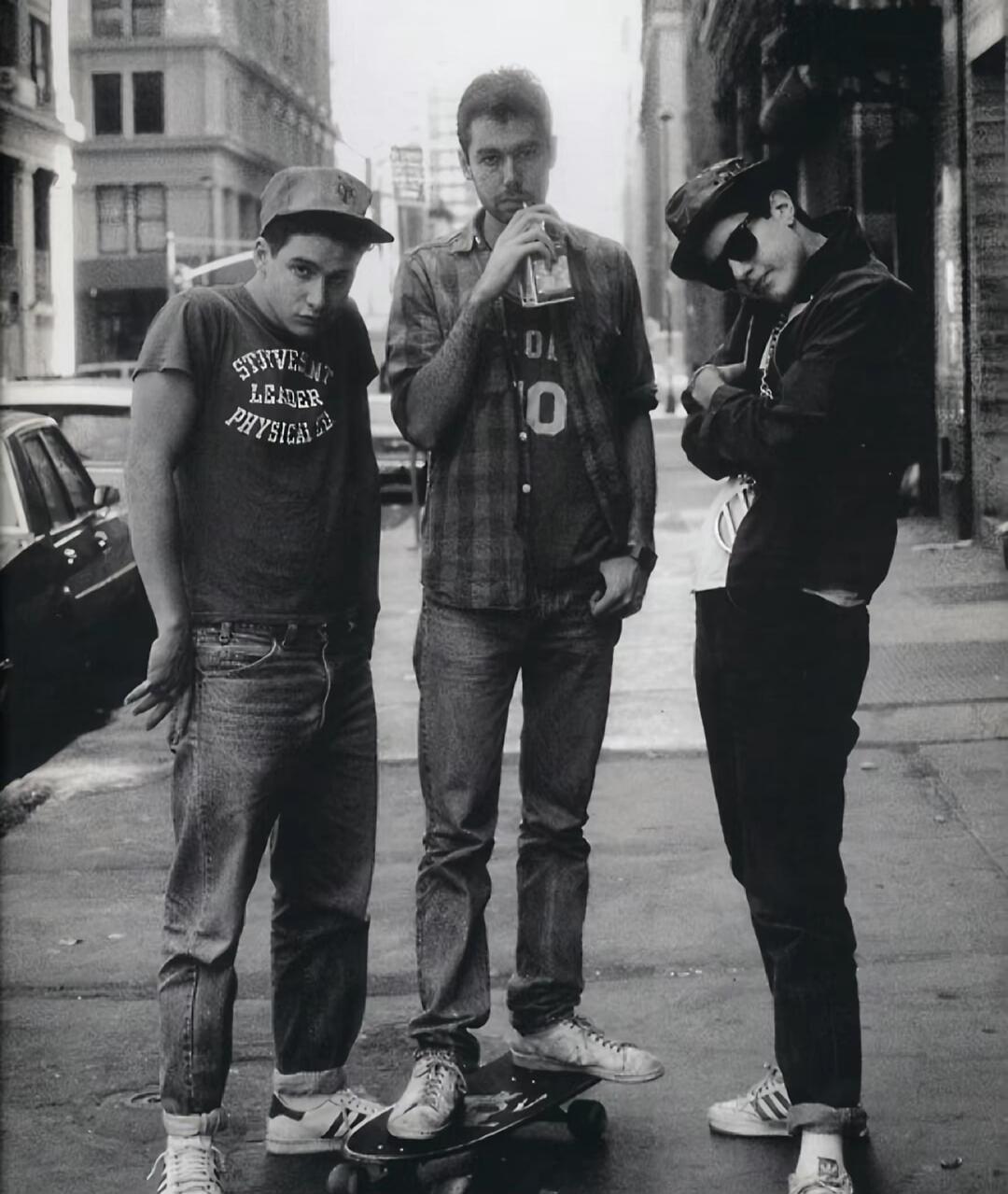 Three young men standing on a city sidewalk with a skateboard.