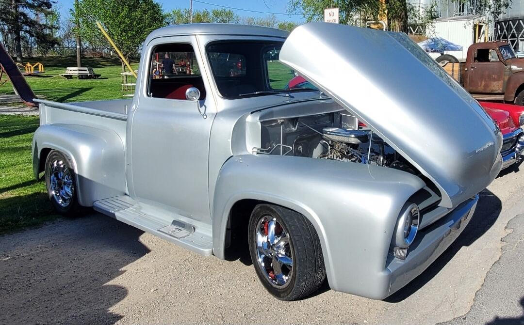 A silver vintage pickup truck with its hood open, on display at a car show.