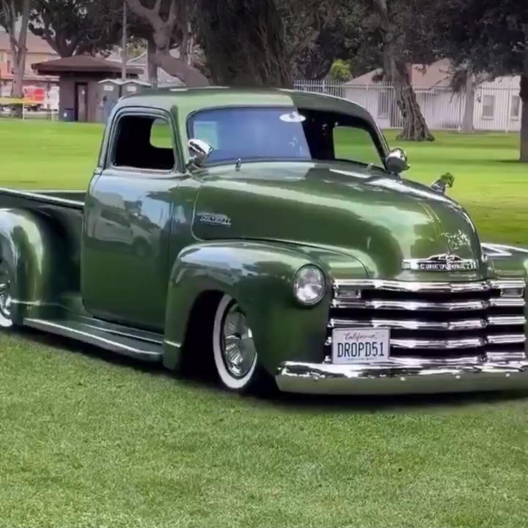 License plate: DROPDS1. Chevrolet emblem on the grille. Vintage green Chevrolet lowrider vehicle parked on grass.