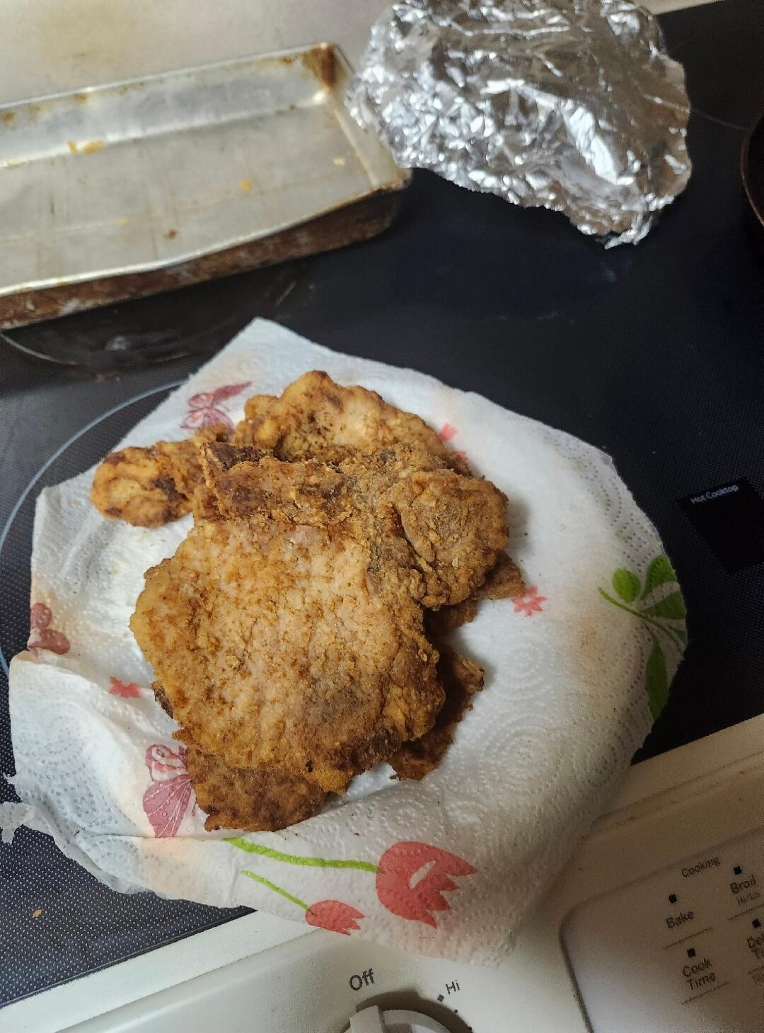 Fried meat resting on a paper towel on a stovetop. Text visible: 'Hot Cooktop', 'Off', 'Hi', 'Cooking', 'Broil', 'Bake', 'Cook Time'.