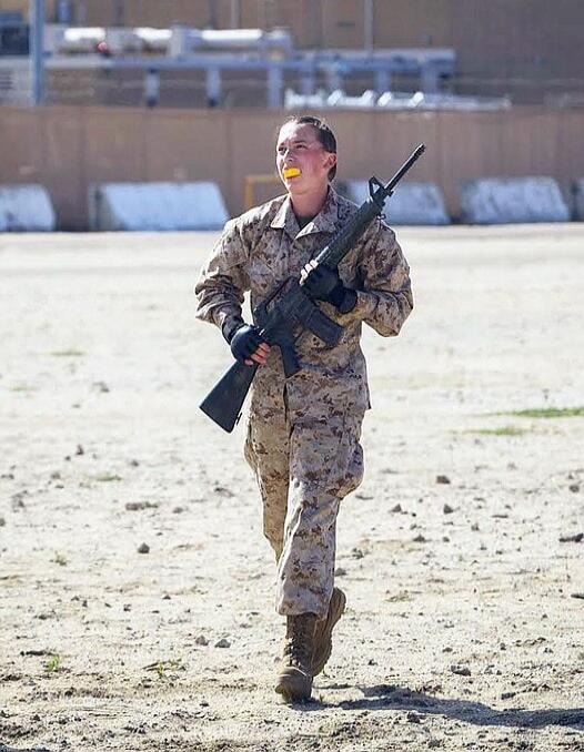 A woman in military uniform with a rifle and a lemon in her mouth.