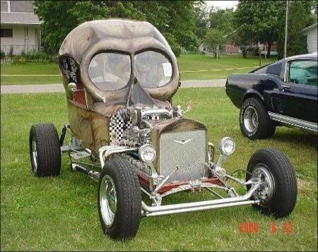 A custom-built hot rod car with a skull-shaped cabin is parked on a grassy field. Another classic car is visible in the background. 2008 6 8