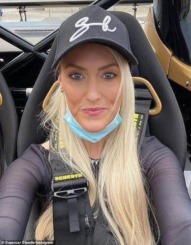 A blonde woman wearing a black cap with an 'SB' logo, a black long-sleeved top, and a face mask pulled down, seated in a racing seat with a SCHROTH harness. The watermark 'Supercar Blondie / Instagram' is visible.