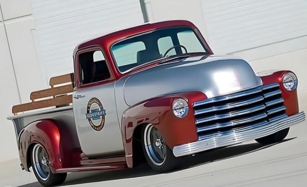 Vintage custom pickup truck with red and silver paint, chrome grille and bumper, whitewall tires.