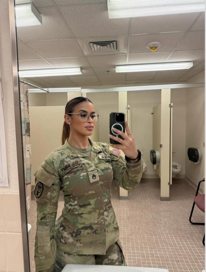 A woman in a US Army uniform, including a Staff Sergeant rank and a Medical Corps patch, takes a mirror selfie in a bathroom. The text 'U.S. ARMY' is visible on her uniform (reversed in the mirror).