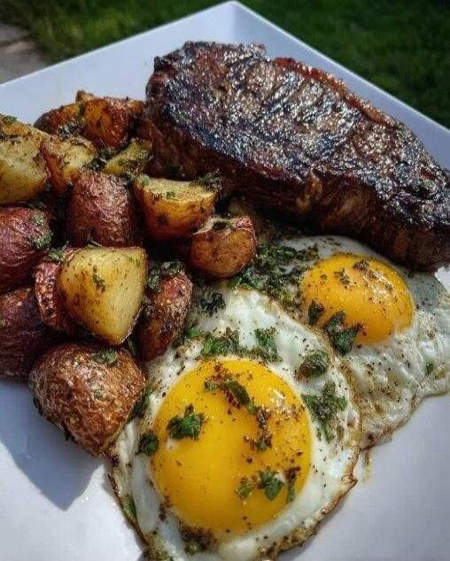 A plate with a grilled steak, roasted potatoes, and two sunny-side-up eggs topped with herbs.