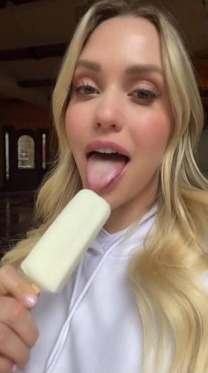 A woman is licking a popsicle with her tongue out.