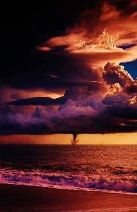 A dramatic sunset over the ocean with a funnel cloud/tornado forming over the water.