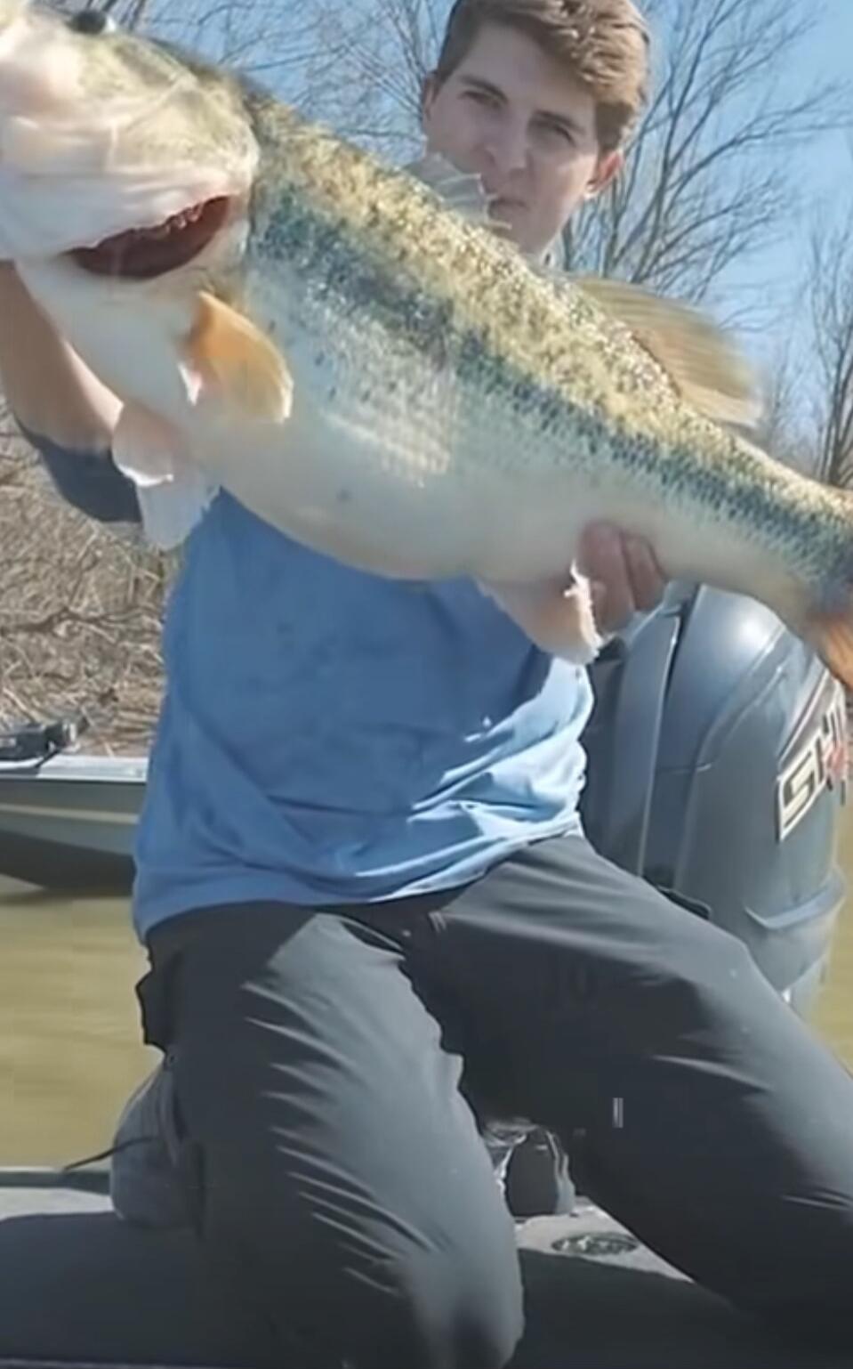 A man in a blue shirt holding a large fish on a boat.