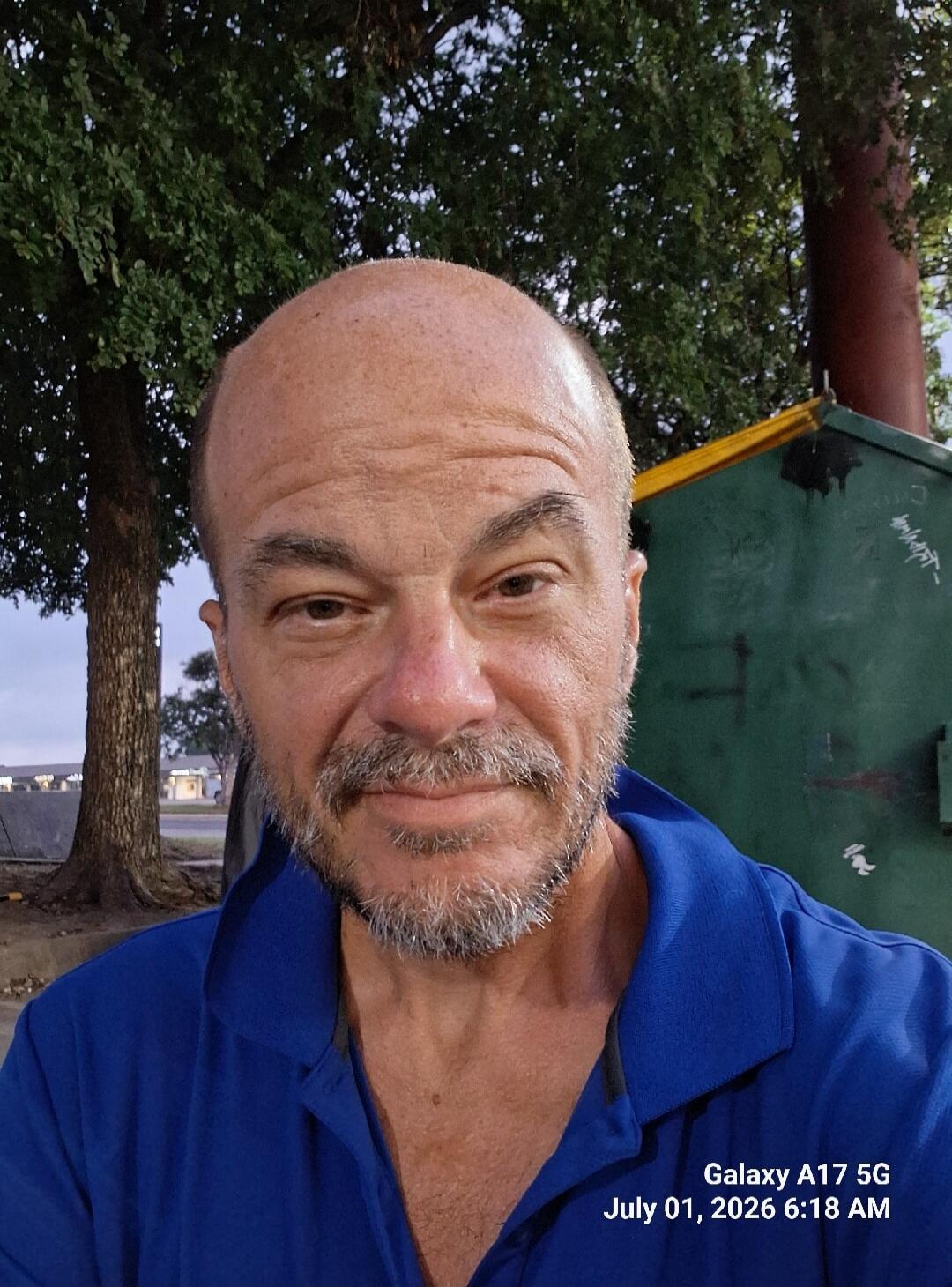 Galaxy A17 5G July 01, 2026 6:18 AM. A man with a beard and a bald head takes a selfie outdoors.