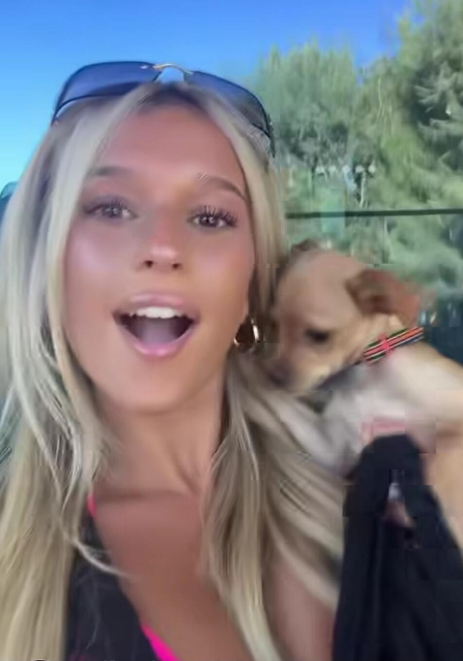 A young blonde woman is holding a small dog and smiling.