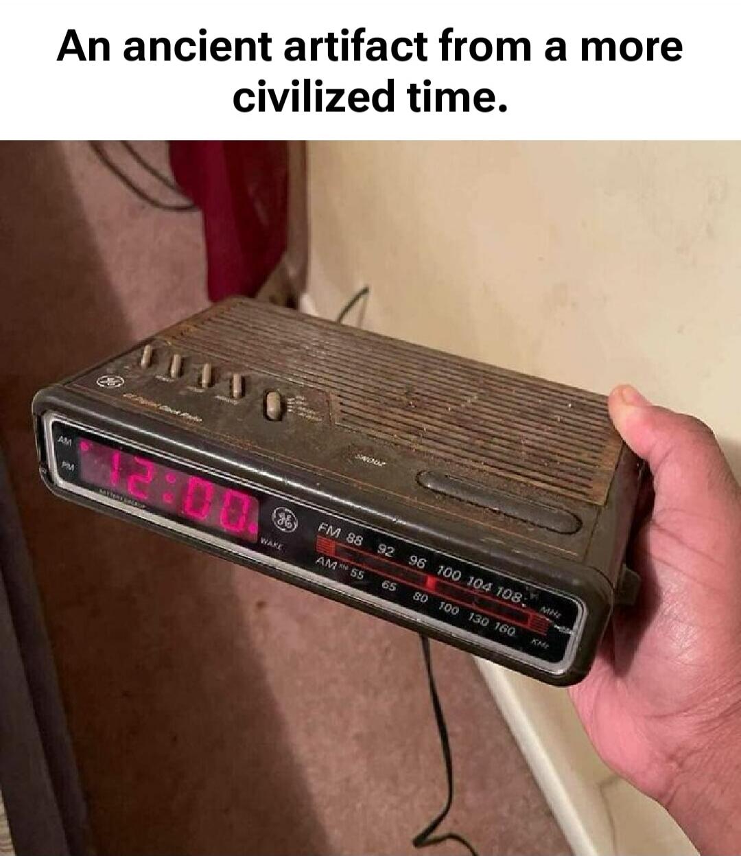 An ancient artifact from a more civilized time. The image shows an old GE digital clock radio displaying 12:00, held by a person.