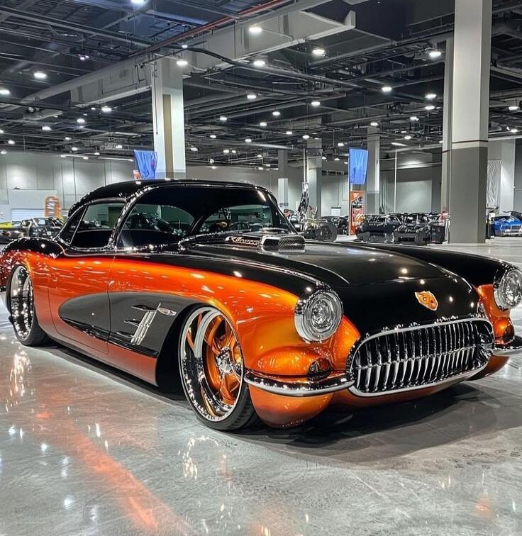 This is a custom Chevrolet Corvette C1, a classic American sports car. It features a striking two-tone paint job with a glossy black top and a vibrant orange lower half, with a gradient effect. The car has been heavily modified with a lowered stance, custom wheels with chrome rims and orange accents, and a prominent hood scoop. The chrome grille an