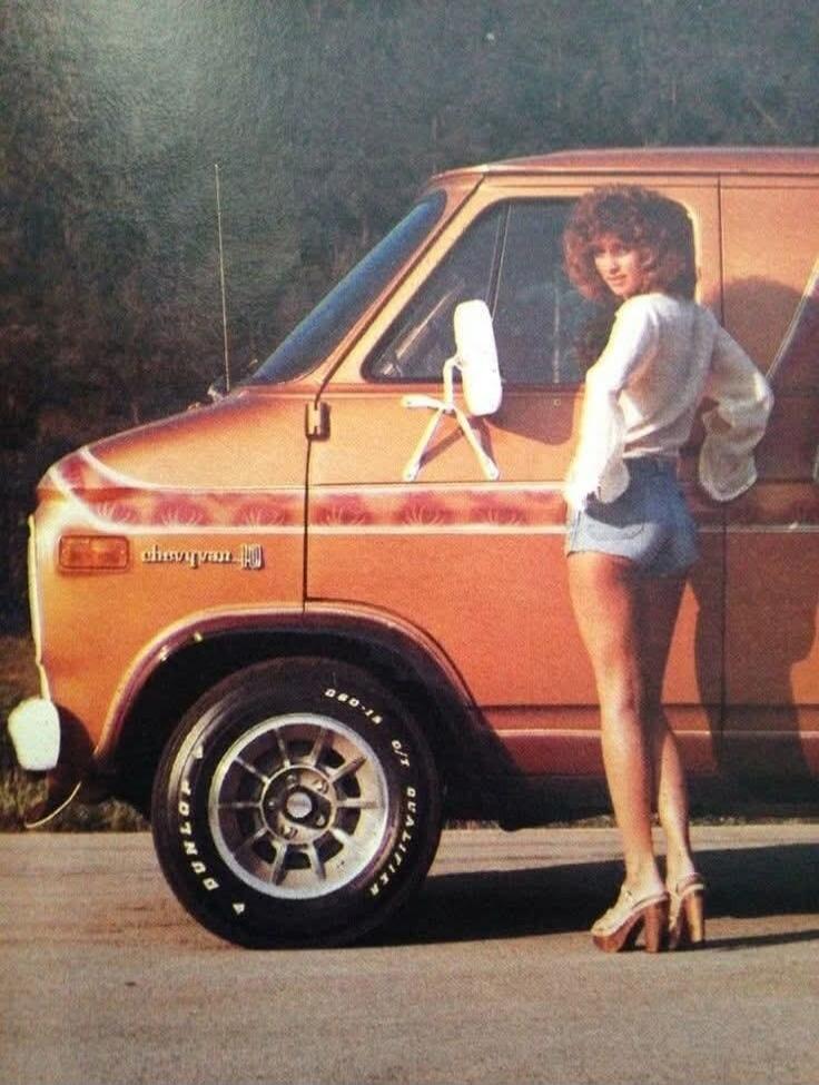 chevyvan DUNLOP QUALIFIER G/T D80-14. A woman in short shorts and a blouse stands next to a customized orange Chevy van, embodying a 70s aesthetic.
