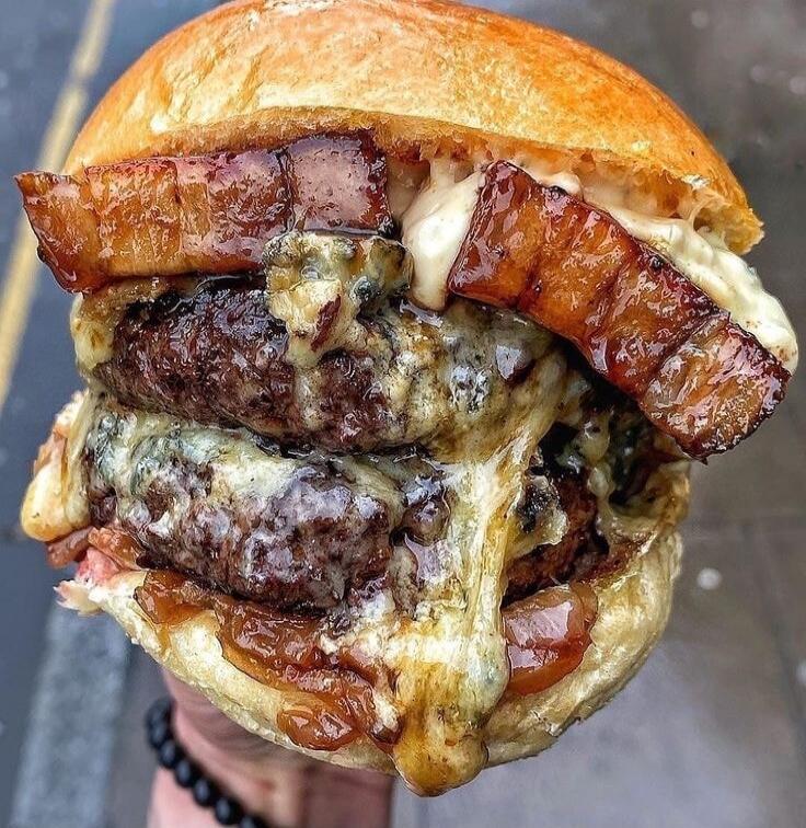 A massive cheeseburger with multiple beef patties, melted cheese, bacon, and a soft bun.