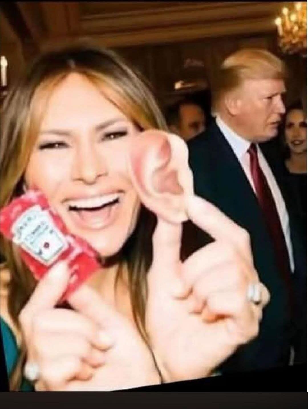 Melania Trump smiling and holding a Heinz ketchup packet and a fake human ear, with Donald Trump in the background.