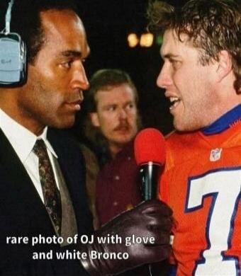 rare photo of OJ with glove and white Bronco. The image shows O.J. Simpson in a suit and headphones, looking at John Elway, who is wearing a Denver Broncos jersey and holding a microphone with a gloved hand.