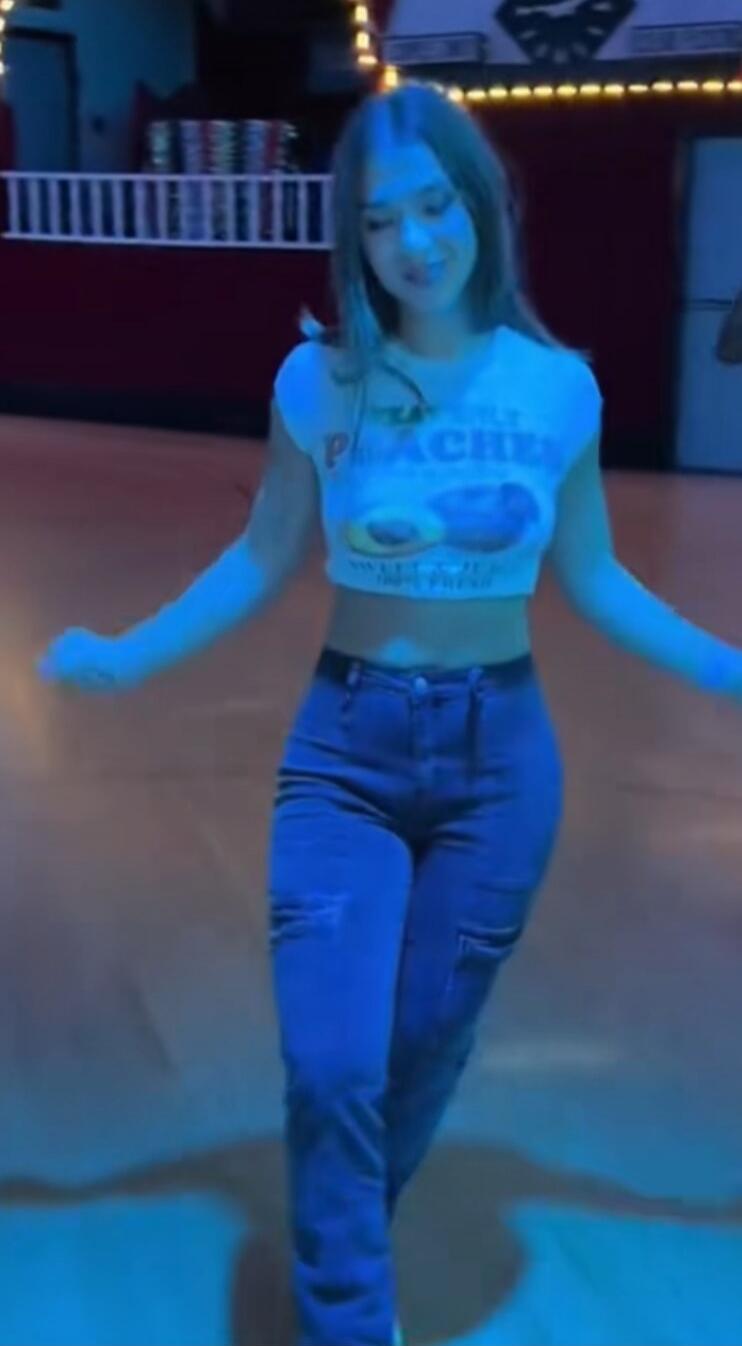 Woman wearing a cropped t-shirt and jeans roller skating in a rink with blue lighting.