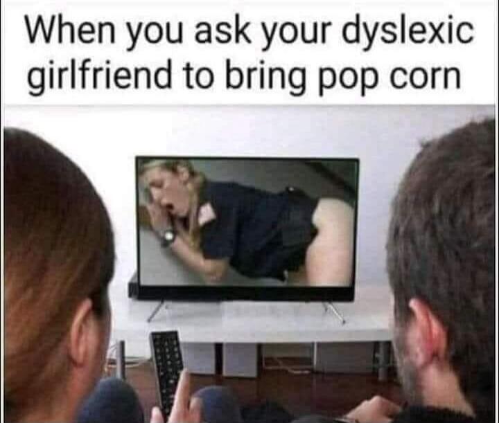 When you ask your dyslexic girlfriend to bring pop corn. A couple is watching TV, and on the screen, a woman is shown in a suggestive, bent-over pose, wearing a dark top and light bottoms.