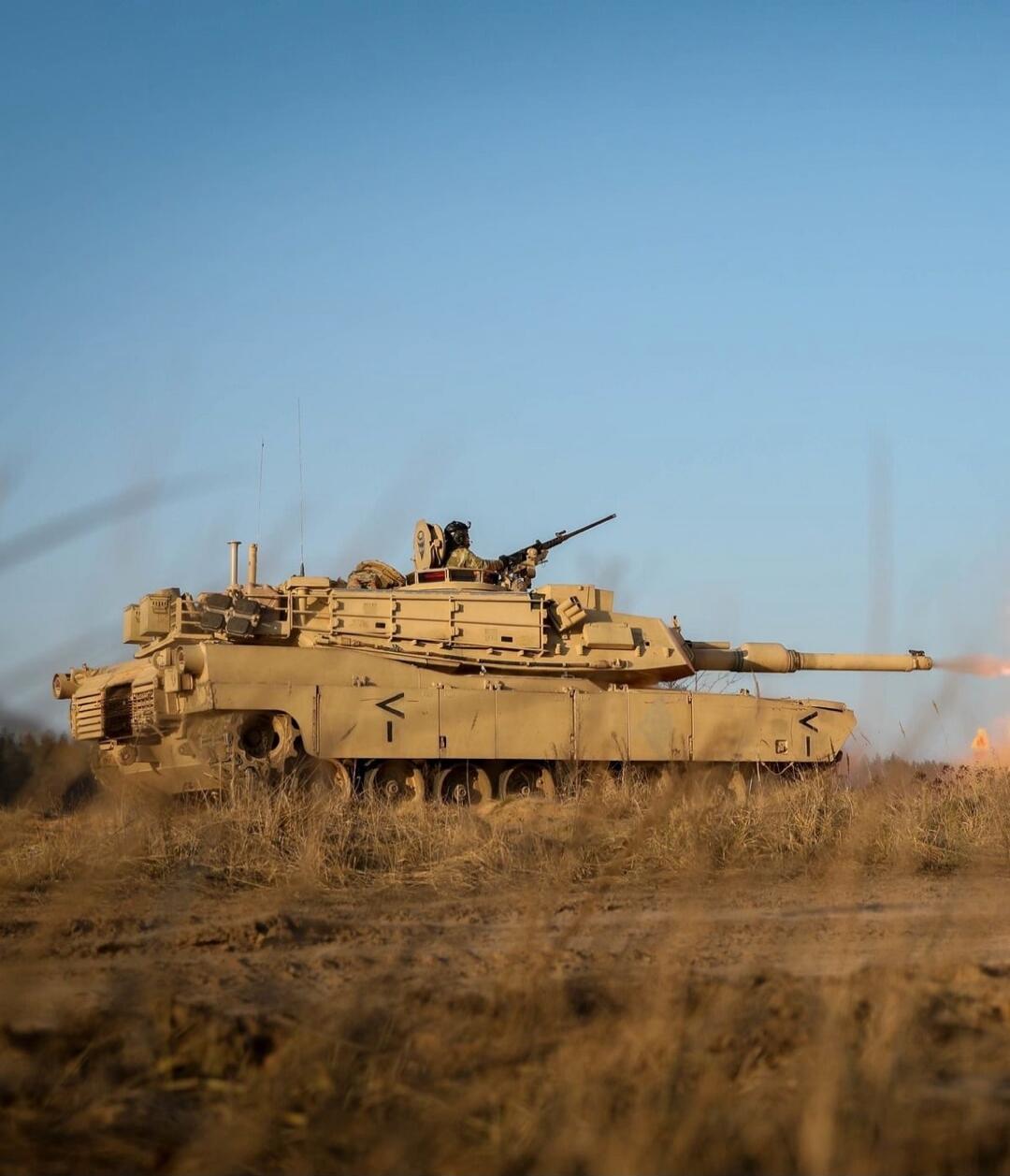 A tan military tank on a grassy field, with soldiers on top.