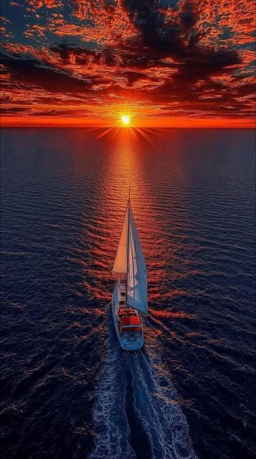 Aerial view of a sailboat on the ocean at sunset.