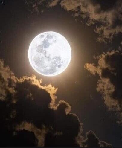 A bright full moon shining in a dark night sky with clouds around it.