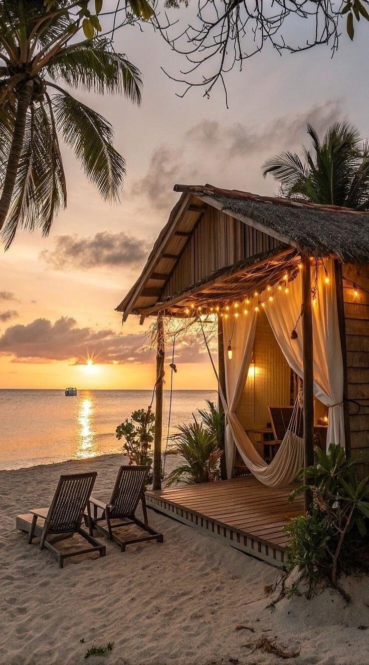 A cozy beach hut with string lights on a sandy shore at sunset.