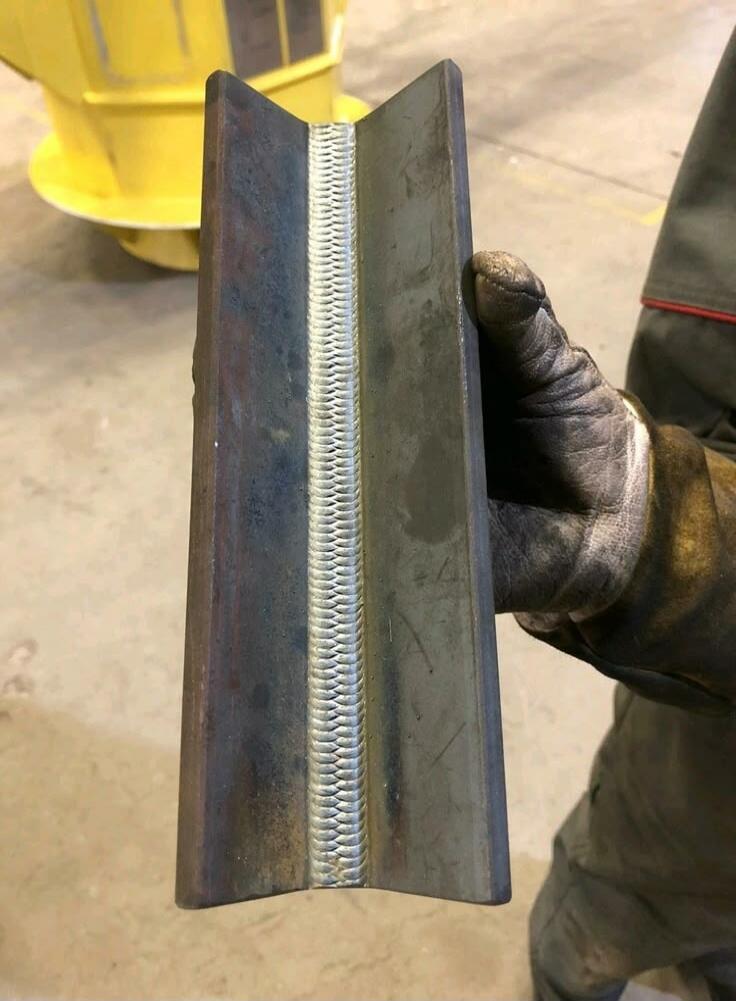 A person wearing a welding glove holds a metal piece with a perfectly executed weld seam.