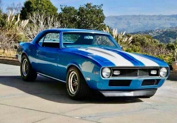 Blue vintage muscle car with white racing stripes parked outdoors.