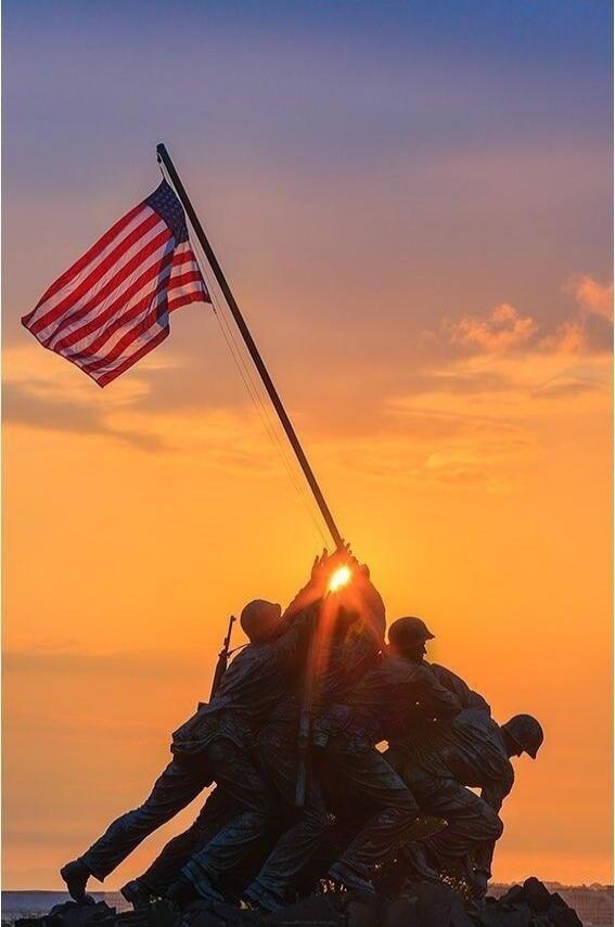 US flag being raised by soldiers at sunset
