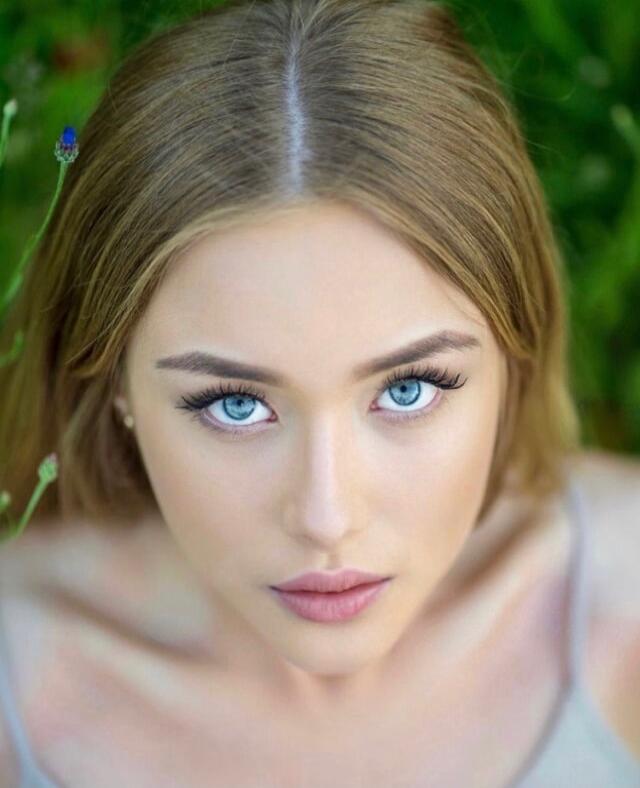 A close-up portrait of a young woman with blue eyes looking up at the camera.