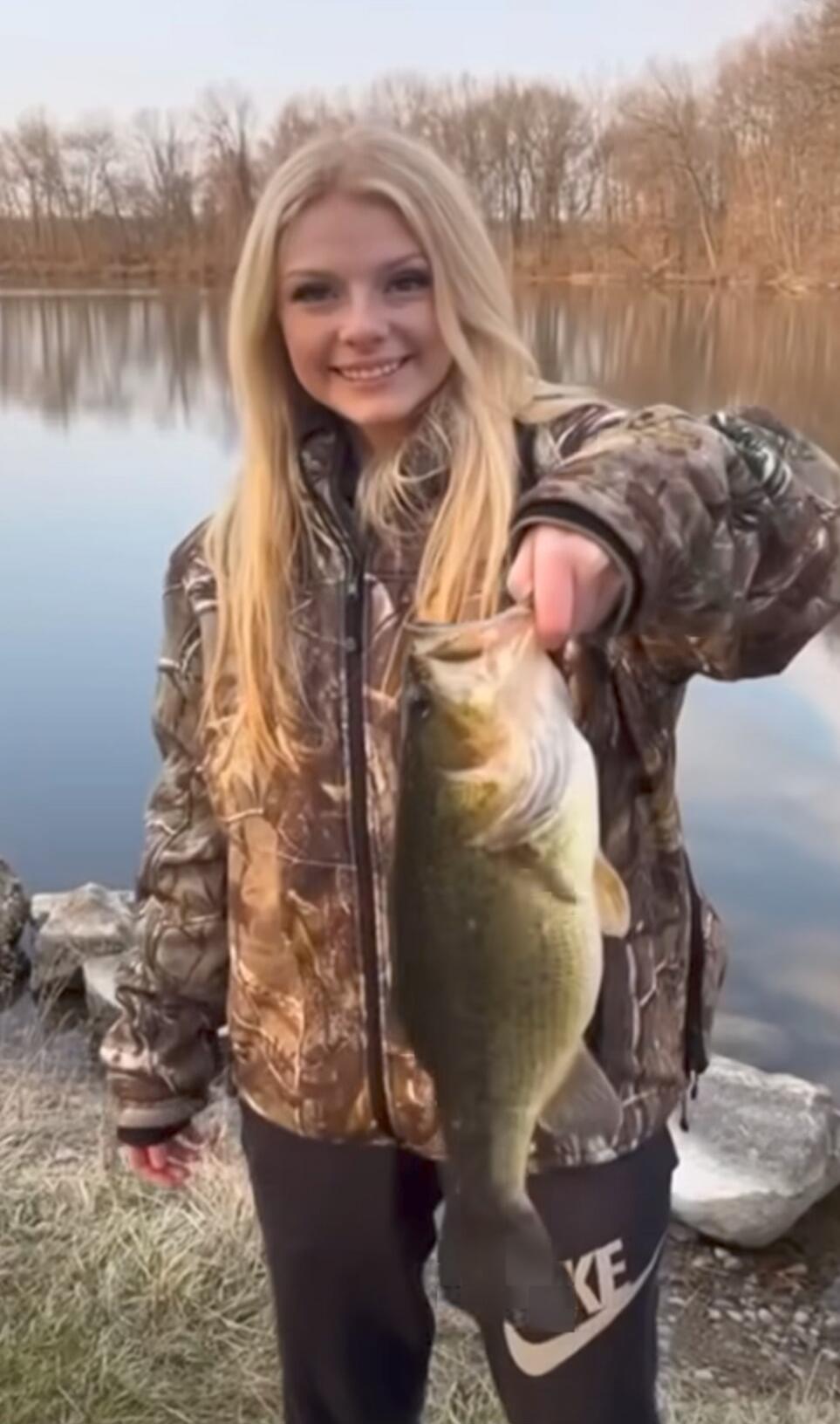 Girl holding a largemouth bass by a lake.