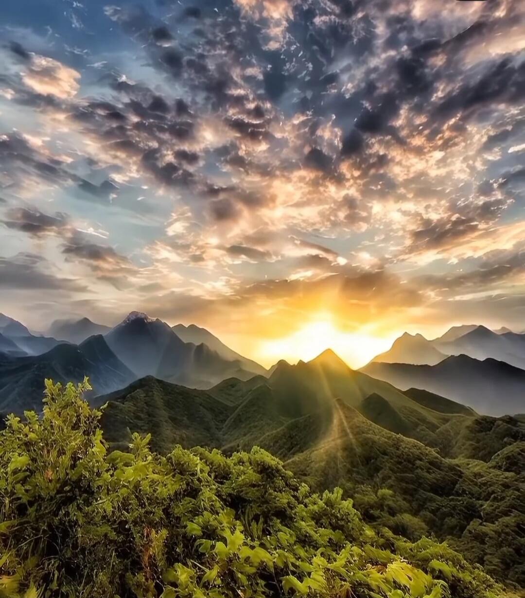 Sunrise over a mountain range with sunlight breaking through clouds.