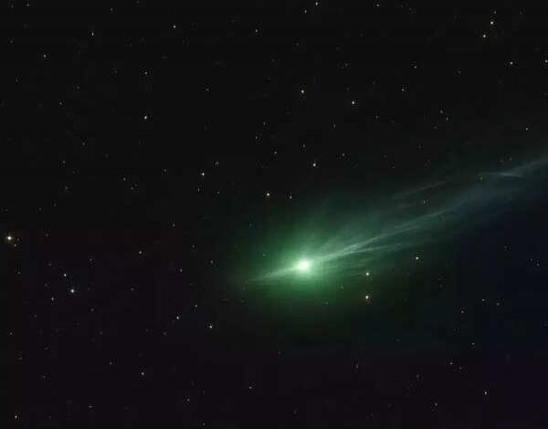 A green comet-like object with a bright nucleus and a trailing tail appears in a starry space background.