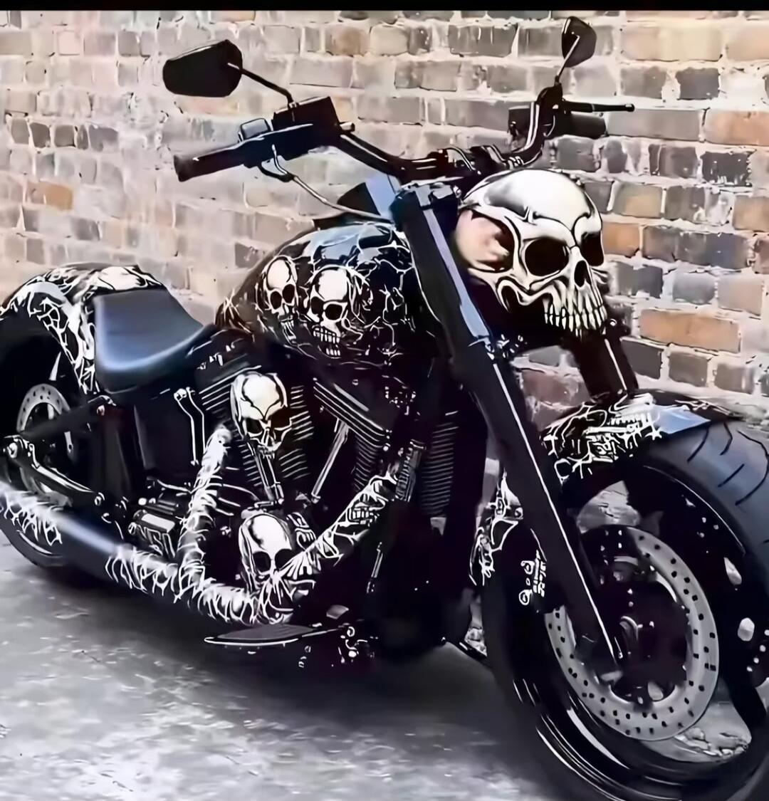 A black motorcycle with extensive skull-themed artwork covering the frame and a skull design on the gas tank and front. The bike features white skull graphics on a dark background, with matching skull patterns on the exhaust and components.