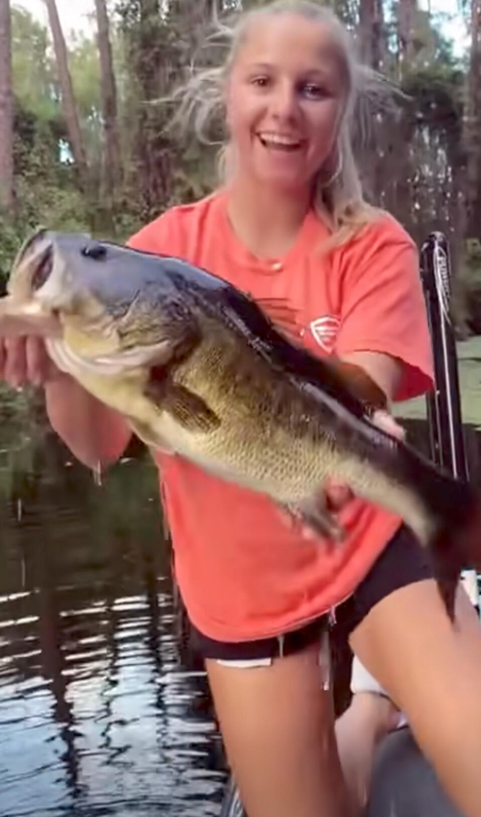 A smiling young woman in an orange shirt holding a large fish on a boat.